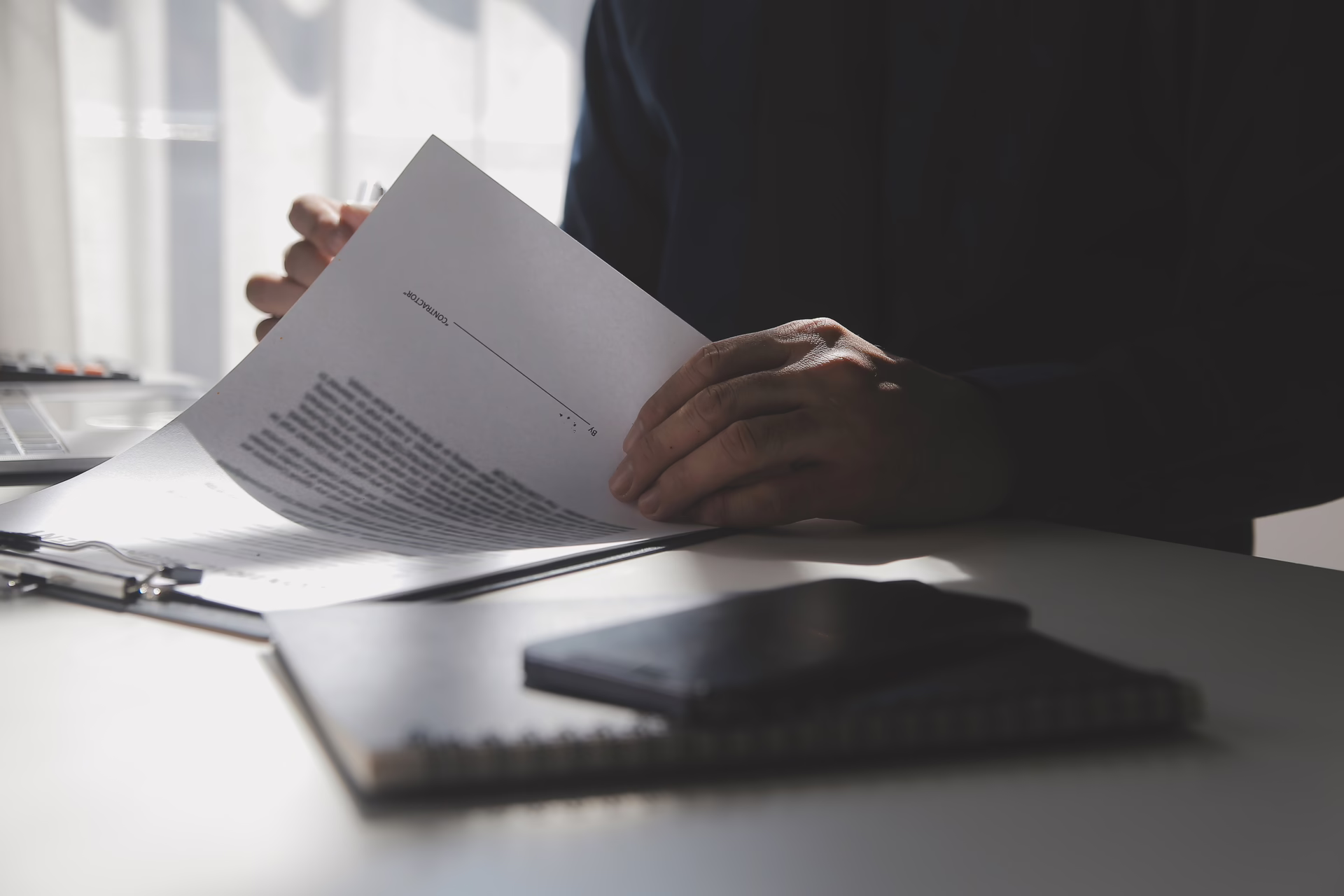 Person reviewing printed documents at a desk with a notebook in a professional office setting.