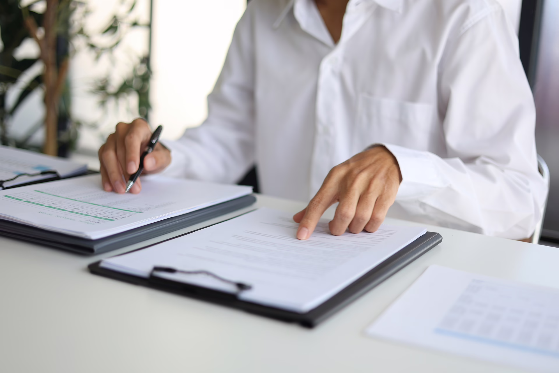 Person reviewing and marking contract documents on clipboards at a desk in a professional office setting.