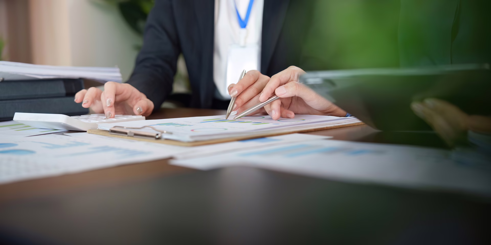 Two professionals reviewing printed documents and financial charts at a desk, with a calculator and files visible.
