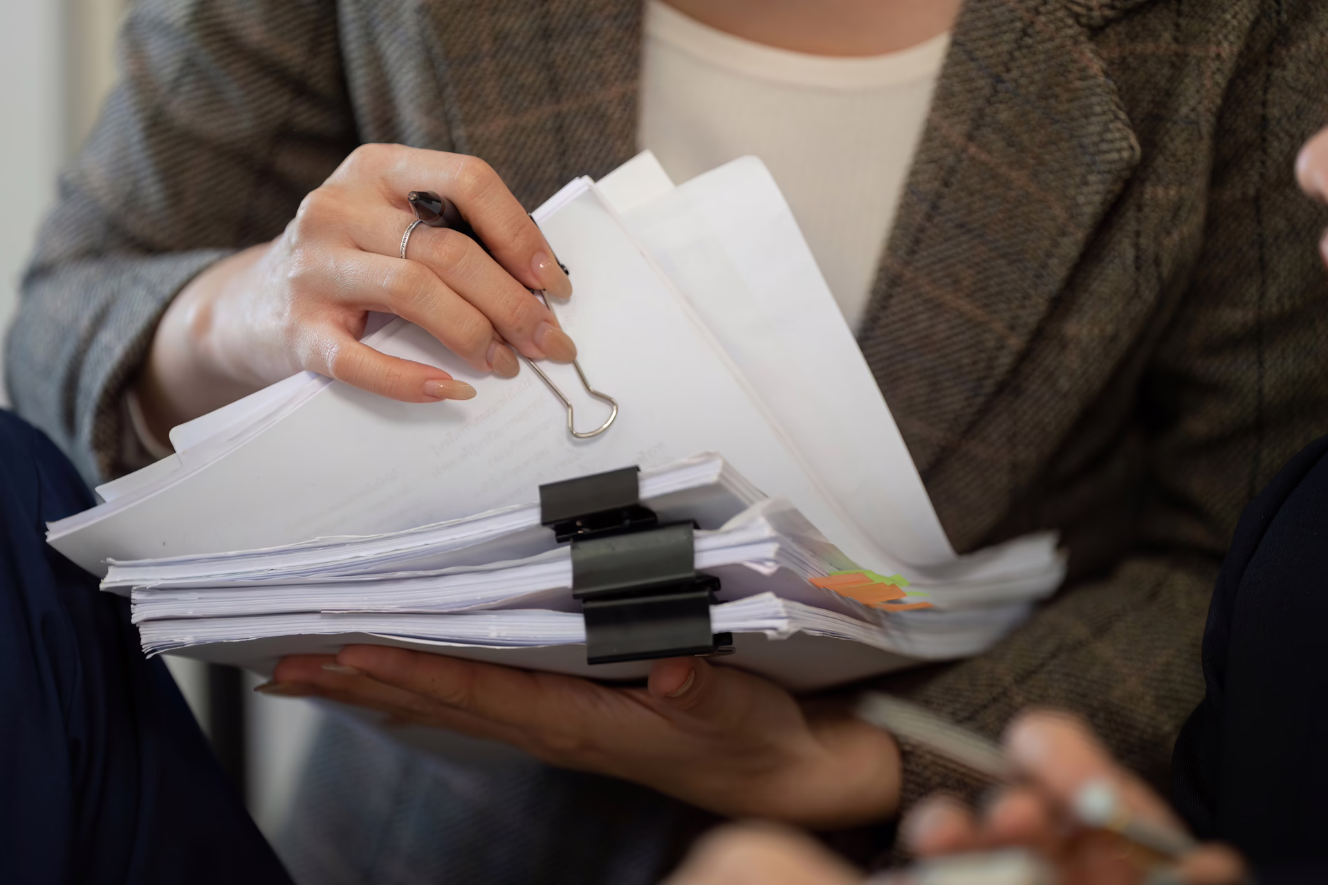 Person holding a thick stack of organised documents clipped together, reviewing paperwork during a professional discussion.